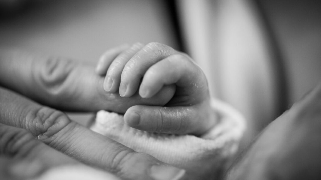 A baby's hand wraps around an adult finger