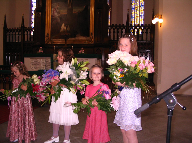 A young Dylan (center) and Nika (right) hold bouquets of flowers at a church.