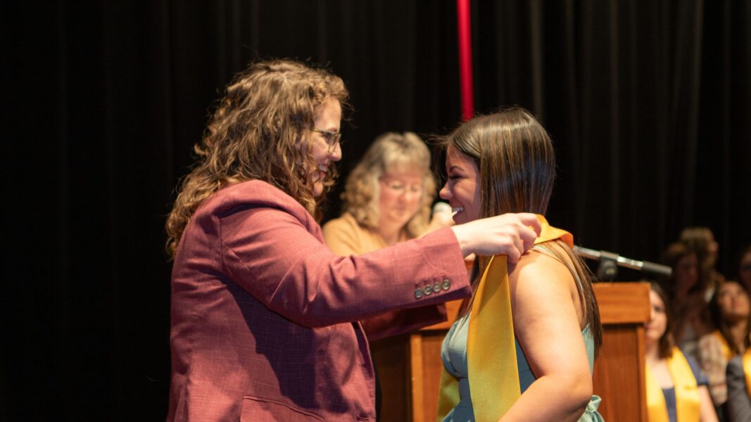 Tyrell places a stole on the shoulders of a 2025 graduate