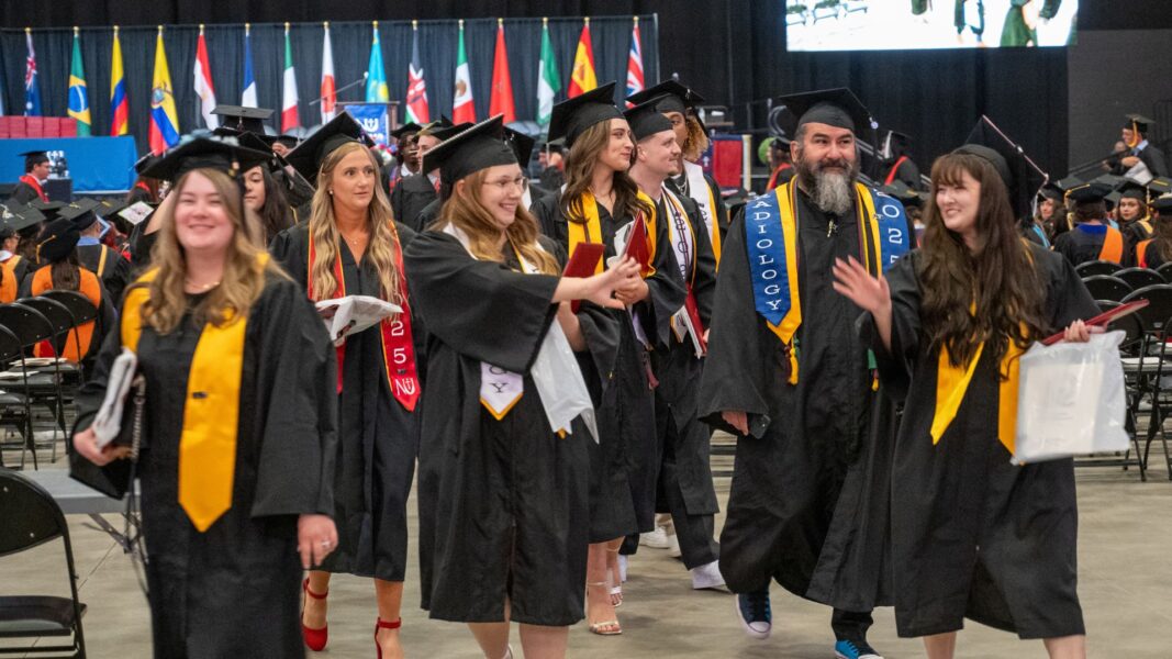 Herd (far right) waves to a fellow graduate on Newman commencement day in May 2025.