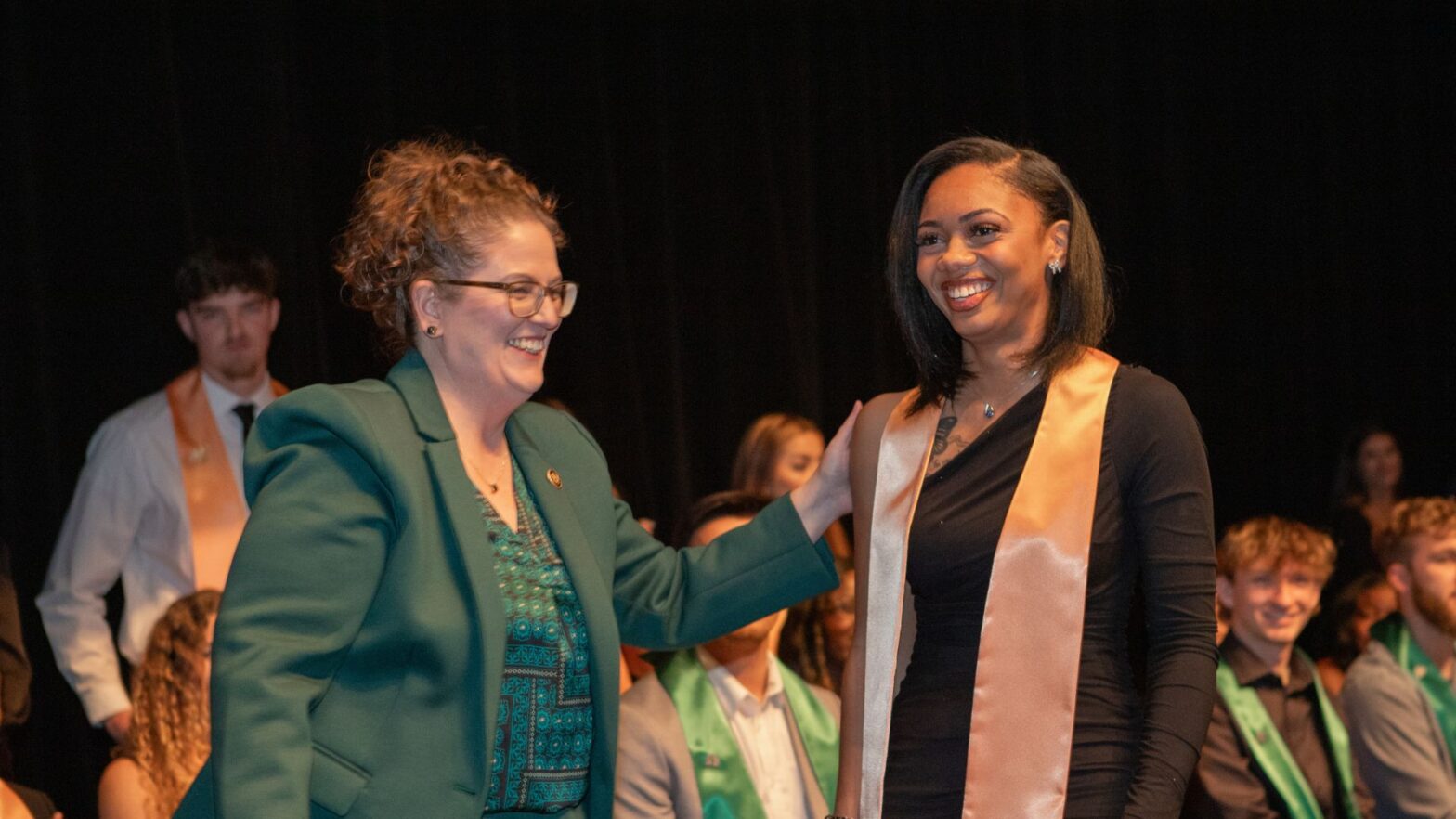Tyrell (left) congratulates a graduate during the annual School of Healthcare Professions pinning ceremony at Newman University.