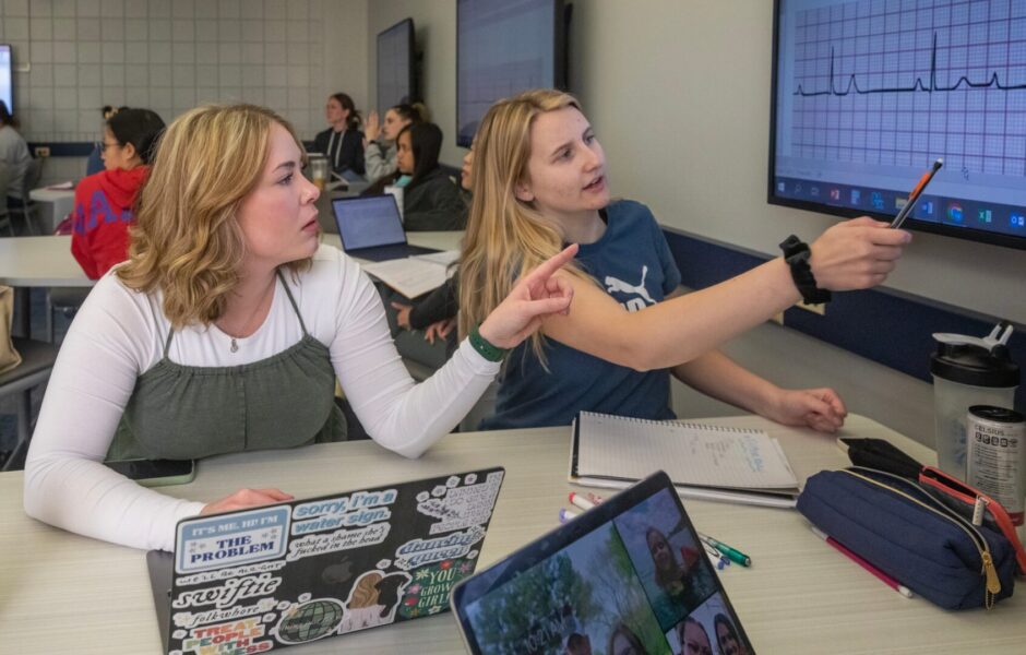 Students in a Newman nursing class study charts on a classroom monitor.