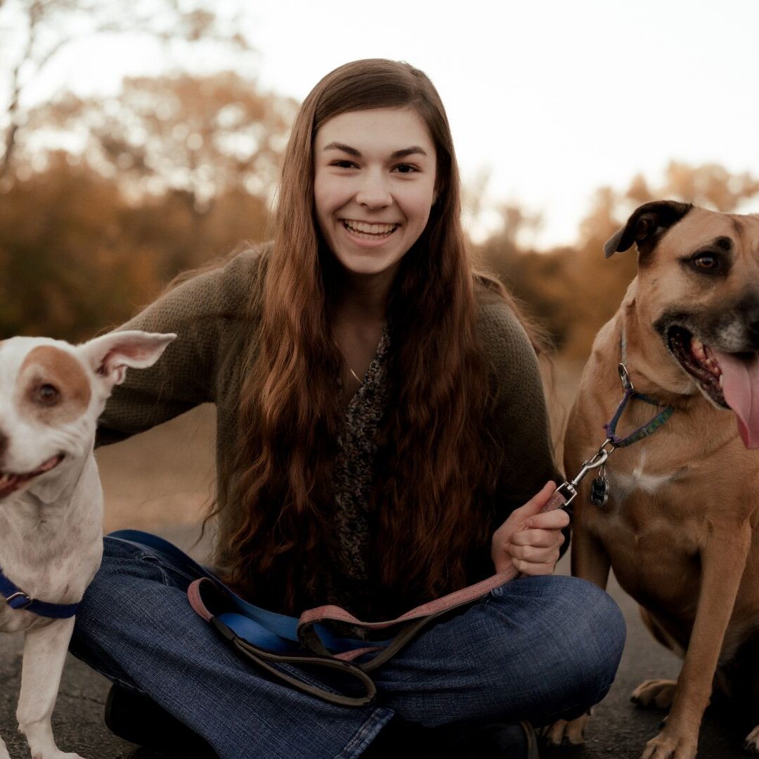 Strickbine sits on the ground with her with two dogs