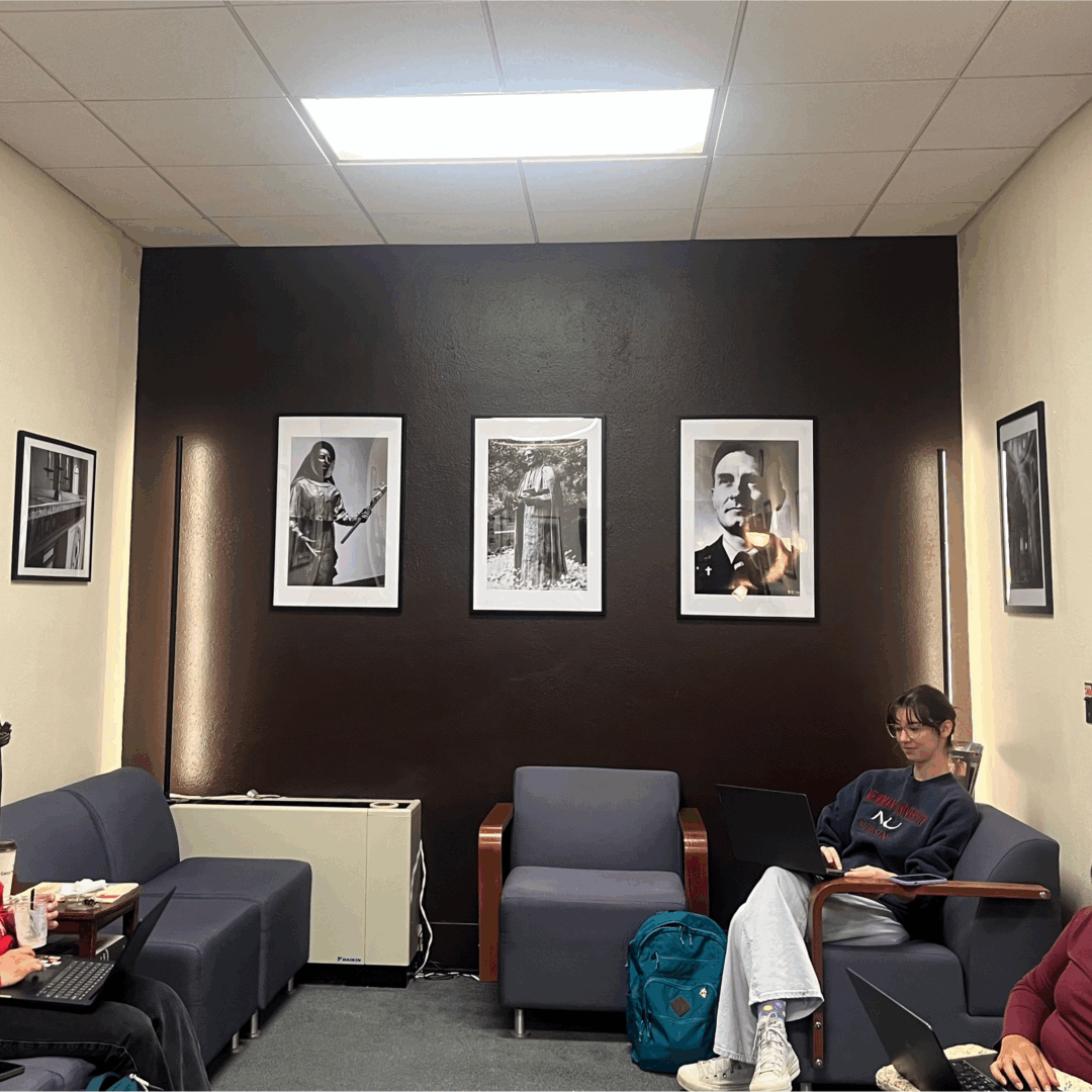 The new Campus Ministry saint wall, a deep brown statement wall in the otherwise white walls, showing only three large framed saint photos.