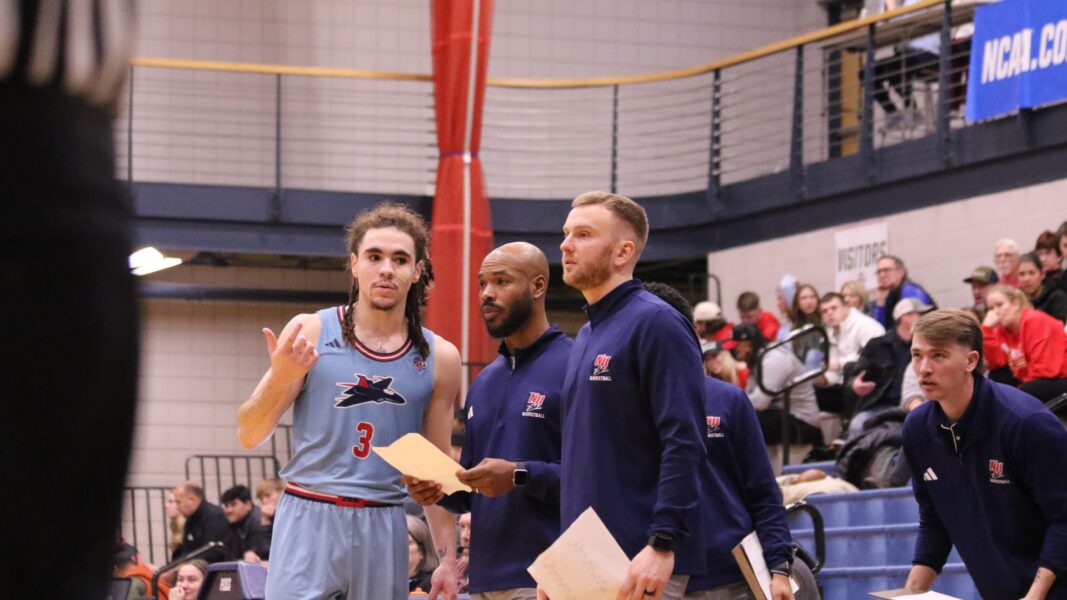 Gosse works with Coach Allen on the sidelines during a men's basketball game.