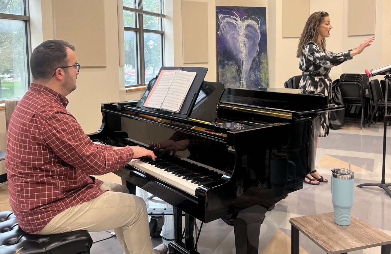 Pictures Pérez on the piano and Swords directing at the front of the room during chorale rehearsal
