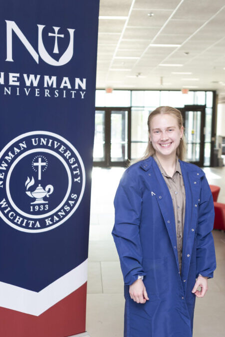 Koenig posing in lab coat in front of Newman banner.