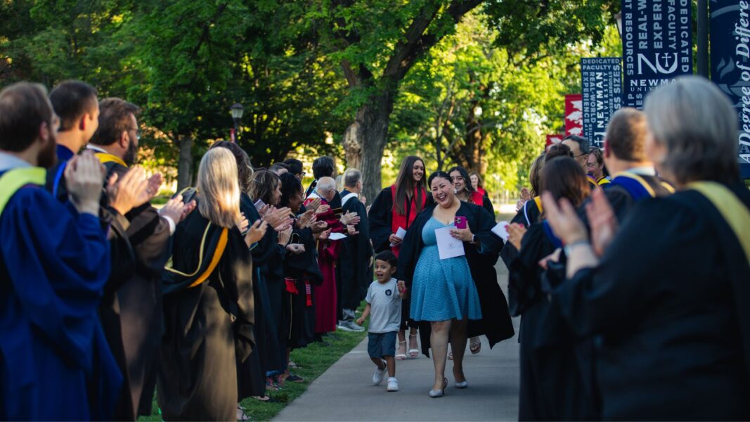 Landa walks down a campus sidewalk lined with Newman staff and faculty following the 2025 Baccalaureate Mass in May.