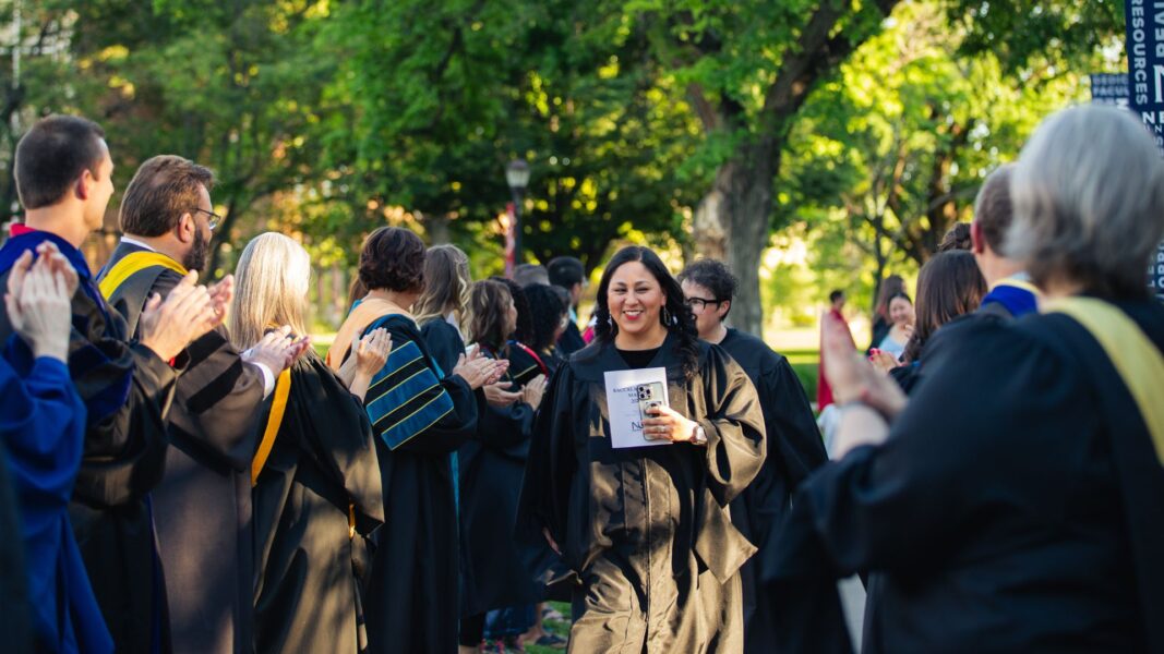 Estrella walks down a campus sidewalk lined by applauding faculty at Newman University.