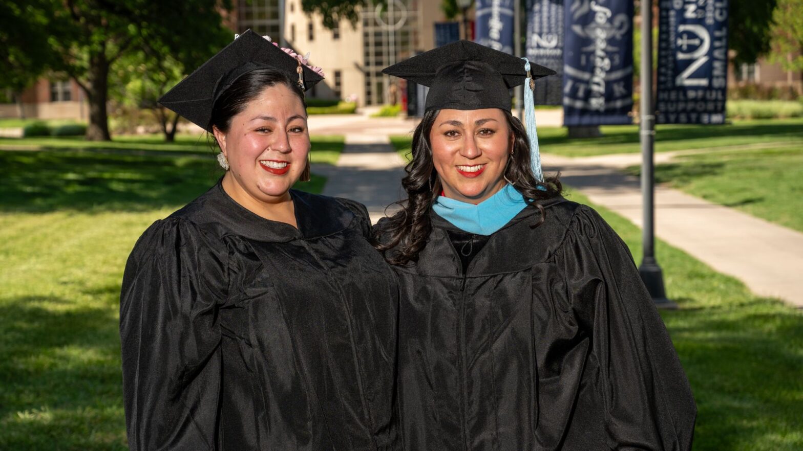 (From left to right) Landa and Estrella wear their graduation caps and gowns for portraits on campus, provided by Newman University.