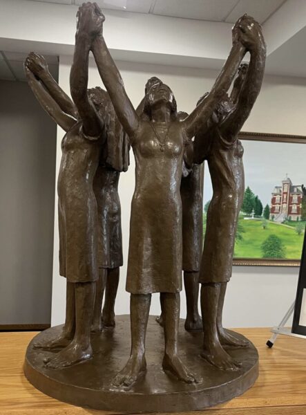 Pictures brown metal sculpture of five women holding hands in a circle