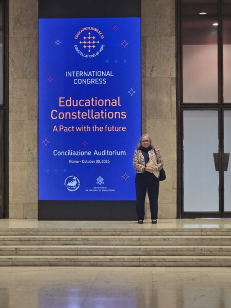 Jagger stands next to a sign that reads "Educational Constellations: A pact with the future" outside the Conciliazione Auditorium.