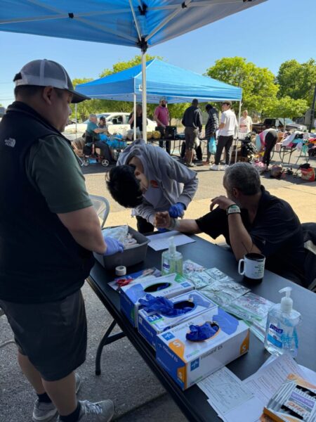 Pictures someone getting blood drawn at a booth at the clinic