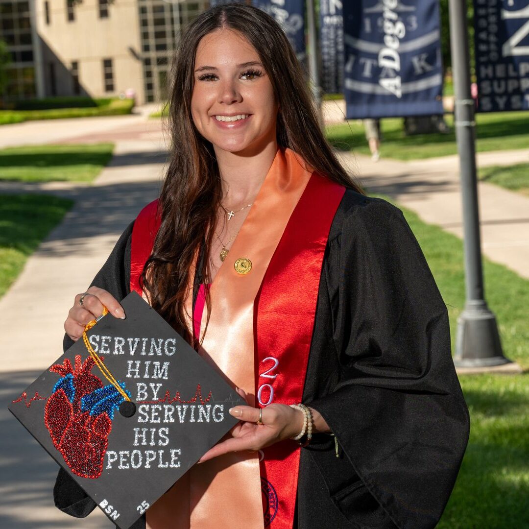 Schaefer holds her graduation cap with "Serving him by serving his people" on Newman's campus.