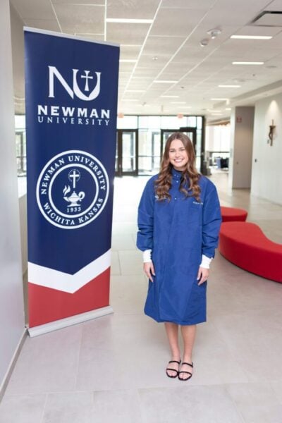 Shows Disbrow in a Newman lab coat, posting next to Newman banner