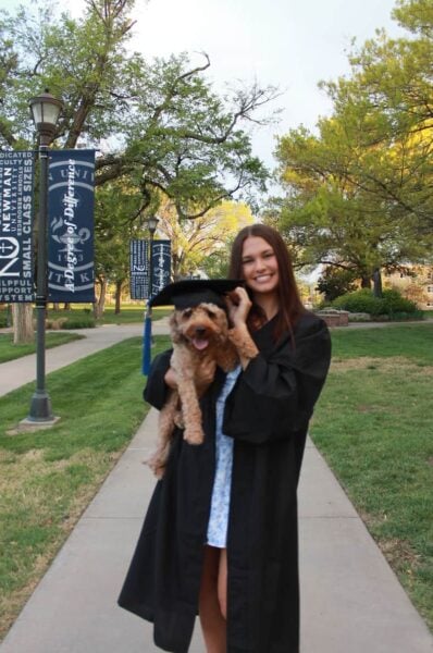 Shows Disbrow in graduation cap and gown, posing with her dog