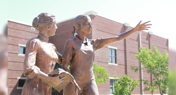 Pictures the sculpture of St. Maria de Mattias, ASC founder, standing with a student reaching toward the future, is located in front of De Mattias Hall