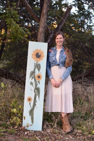Strickbine stands beside her painting of a sunflower.