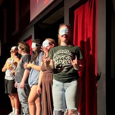Donning a face mask, McGrath looks to the camera while onstage at Backline Comedy Theatre in Omaha.