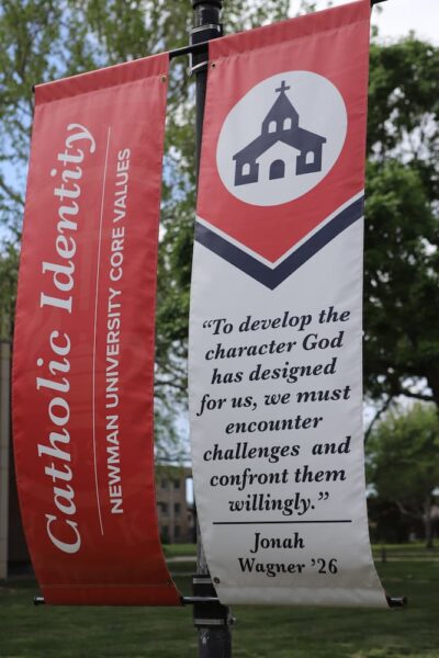 A Newman pole banner quotes a graduate, Jonah Wagner, and encourages students to "encounter challenges and confront them willingly."