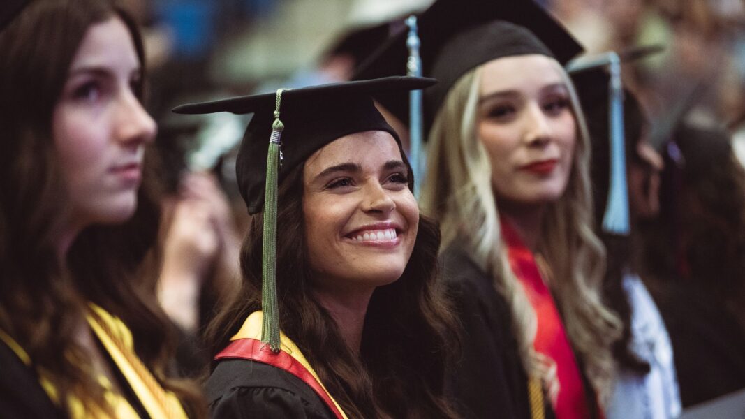 Graduates smile from their seats.