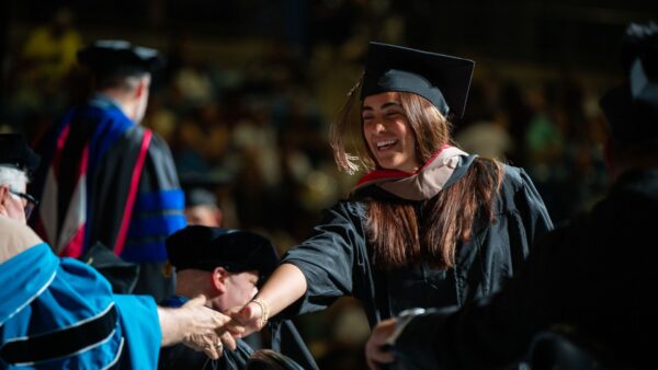 A 2026 graduate smiles as she crosses the commencement stage during Newman's graduation ceremony.