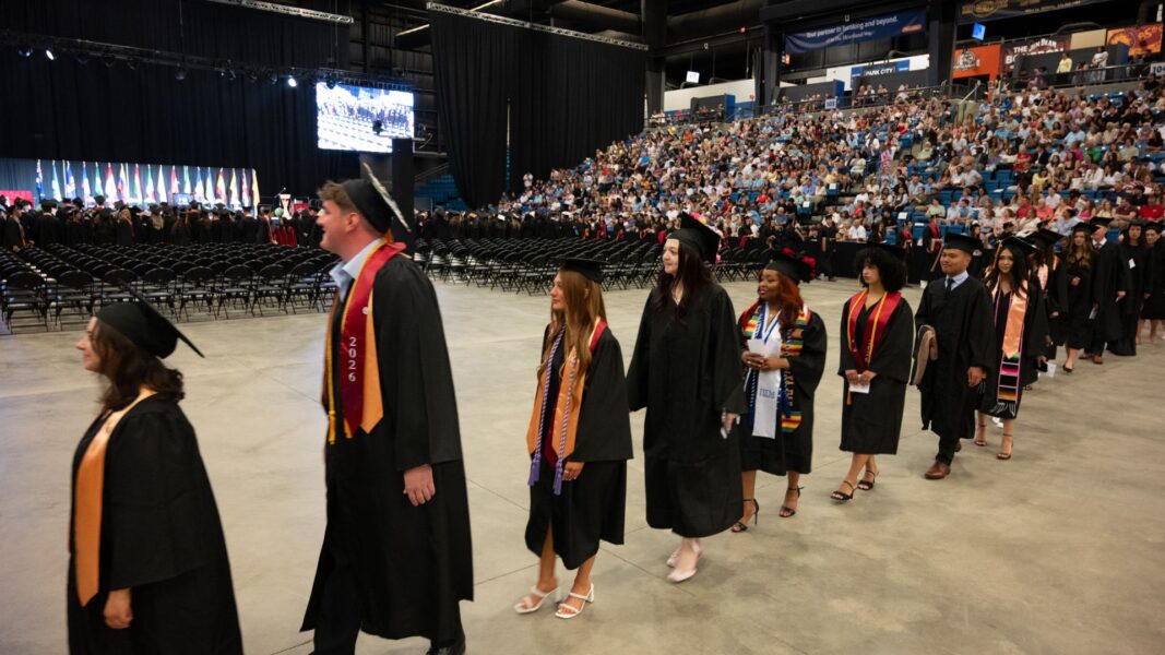 Simons (second from left) walks with fellow graduates through the Heartland Credit Union Arena on Newman University commencement day.