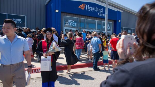 A graduate's family member takes a polaroid photo of her in front of the Heartland Credit Union Arena on Newman's graduation day.