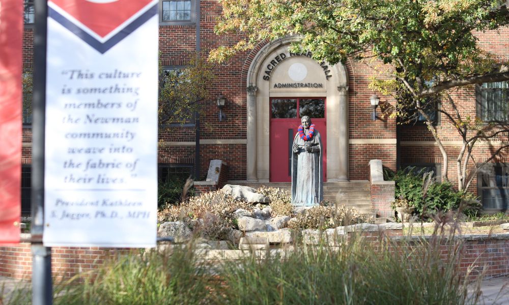 A campus shot of the St. Newman sculpture outside of Sacred Heart Hall